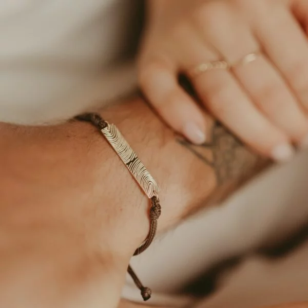 Vrouwenhand op een arm die een mannen armband met bar draagt